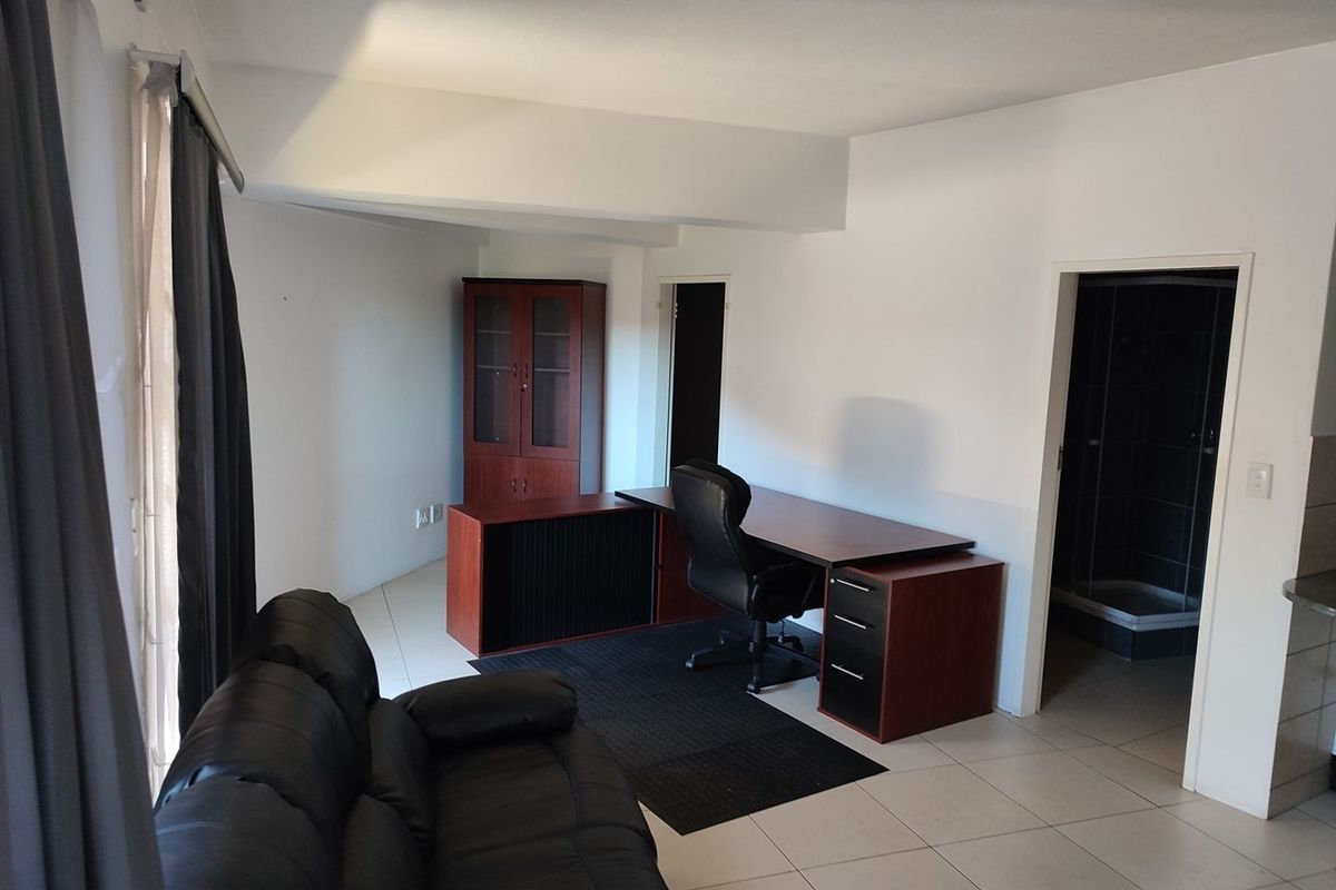 A functional office space featuring neutral tiled flooring and direct access to an adjacent bathroom area.