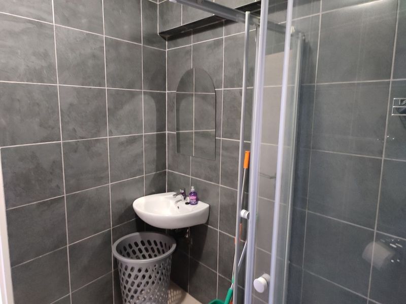 A compact bathroom featuring dark grey wall tiles, a wall-mounted basin, and a glass shower enclosure.