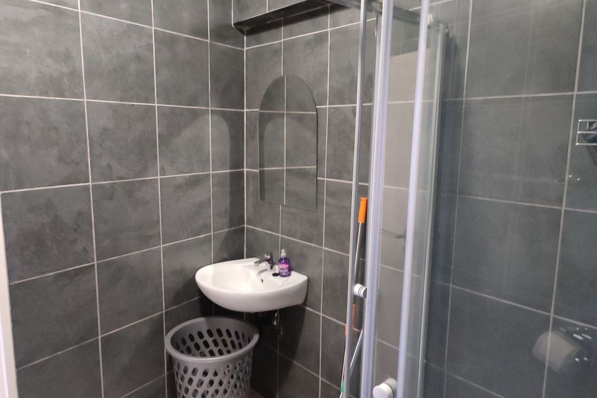 A compact bathroom featuring dark grey wall tiles, a wall-mounted basin, and a glass shower enclosure.