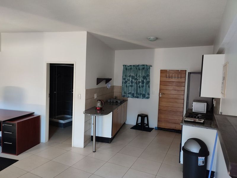 Open-plan kitchen area featuring built-in cabinetry, stone countertops, and tiled flooring, with direct access to an adjacent bathroom.