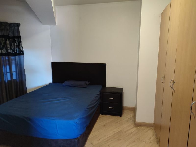 A bedroom featuring light-toned laminate flooring and a built-in wooden wardrobe.
