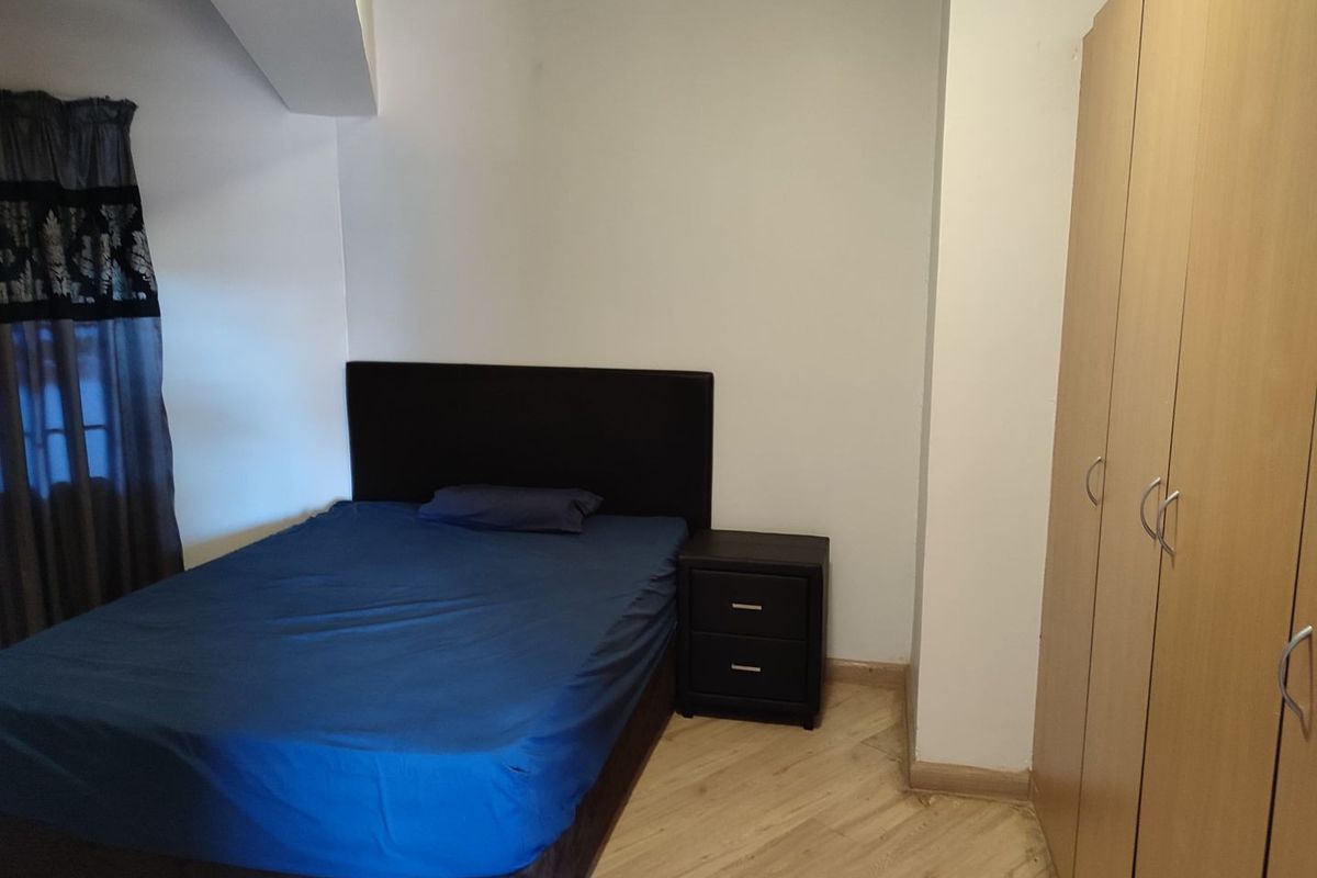 A bedroom featuring light-toned laminate flooring and a built-in wooden wardrobe.