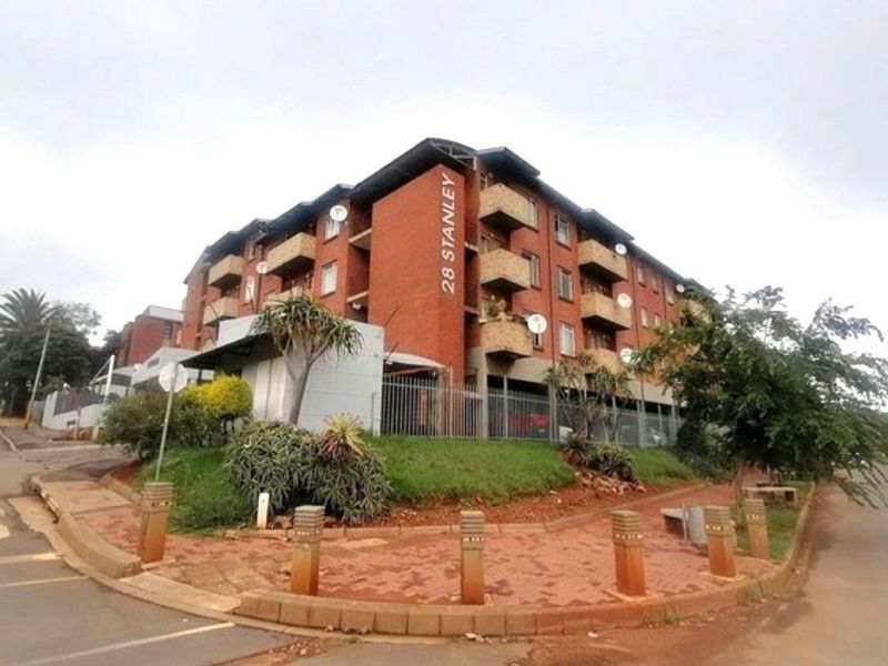 Exterior view of the apartment building facade featuring brick construction, multiple balconies, and perimeter security fencing.