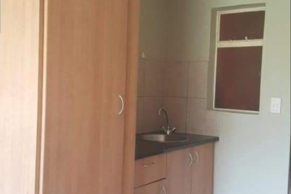 A compact kitchen area featuring light wood-finish cabinetry, a stainless steel sink, tiled backsplash, and neutral tiled flooring.