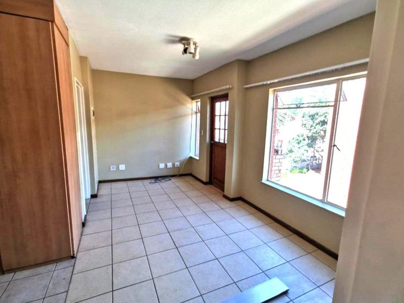 An empty living area featuring tiled flooring, built-in storage cupboards, and large windows providing natural light.