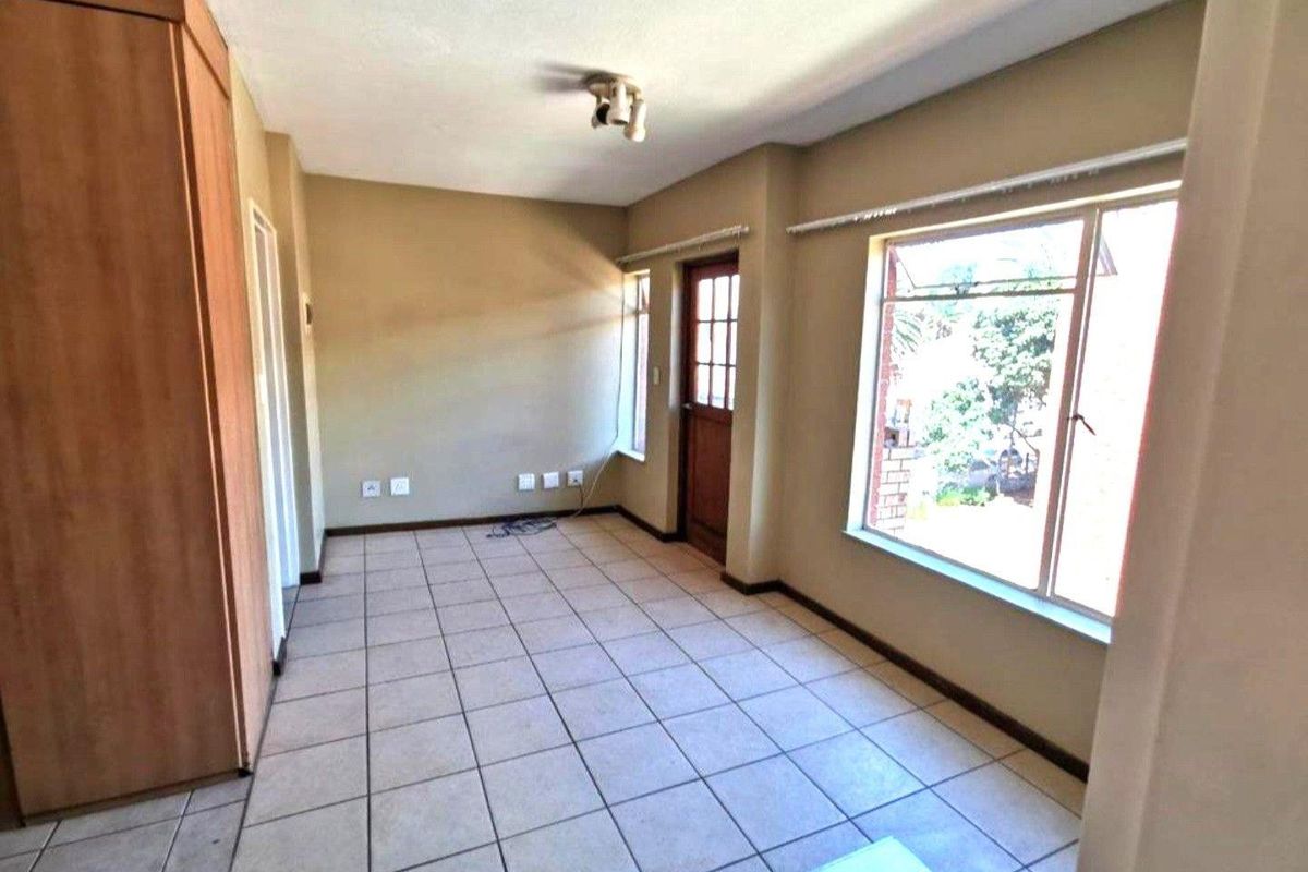 An empty living area featuring tiled flooring, built-in storage cupboards, and large windows providing natural light.