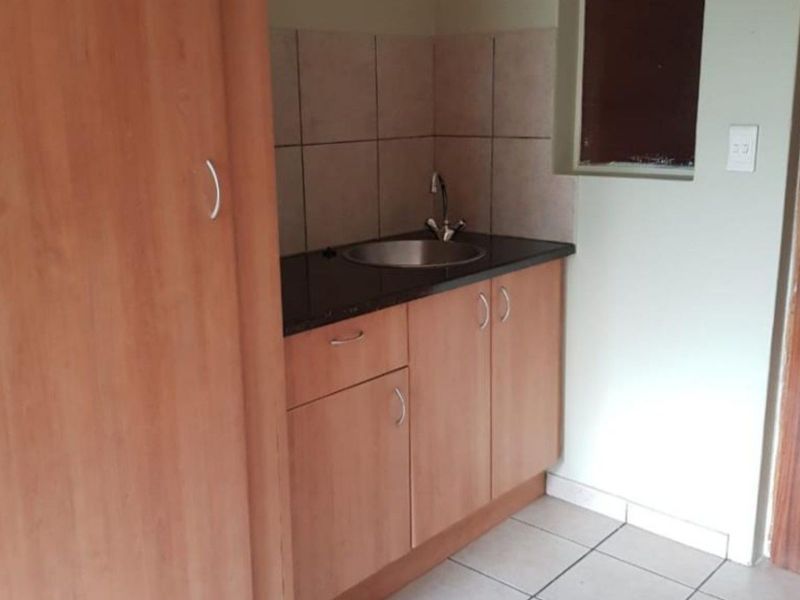 A compact scullery area featuring built-in wooden cabinetry, a dark stone countertop, and a stainless steel sink with tiled splashback.