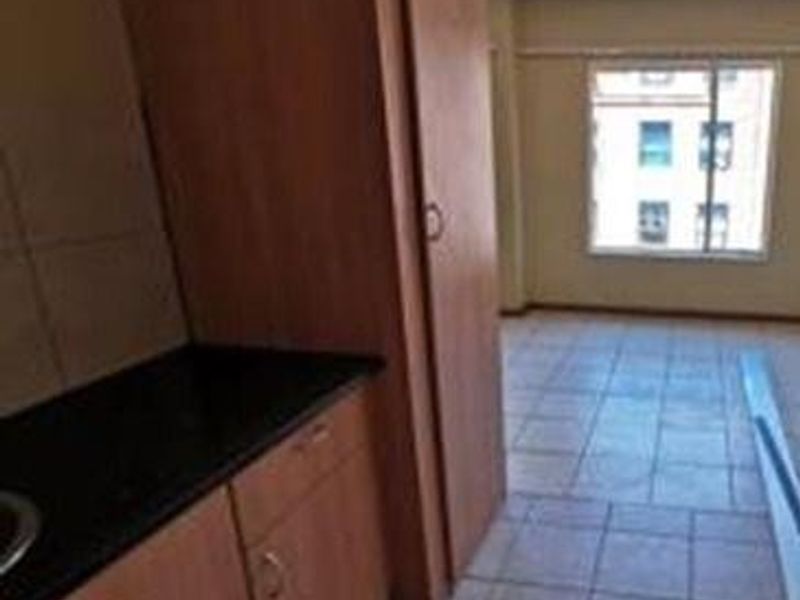 A compact, empty kitchen area featuring dated built-in cabinetry, dark countertops, and tiled flooring, offering potential for a modern renovation.