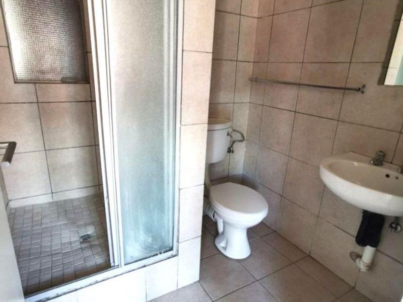 A functional bathroom featuring a shower enclosure, toilet, and wall-mounted basin with tiled finishes throughout.