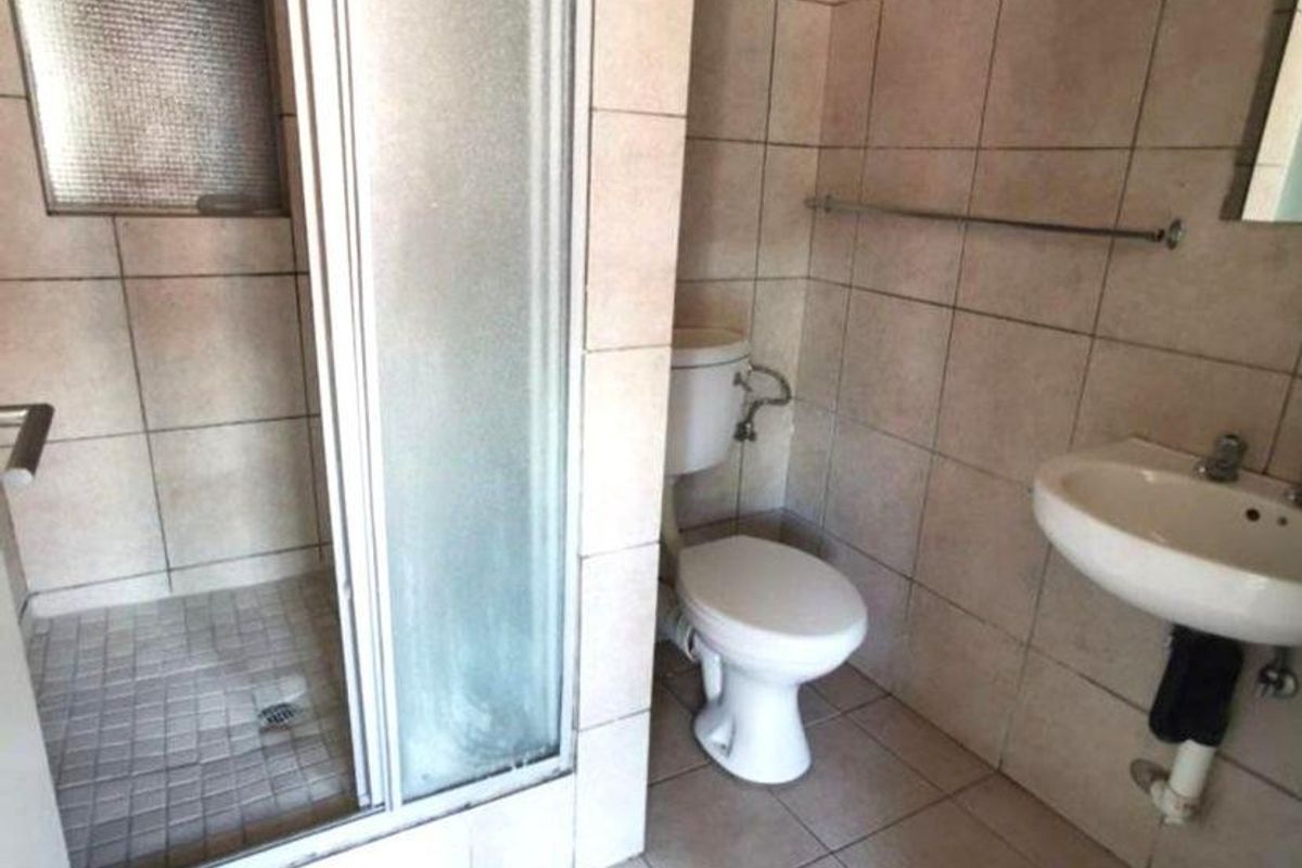 A functional bathroom featuring a shower enclosure, toilet, and wall-mounted basin with tiled finishes throughout.