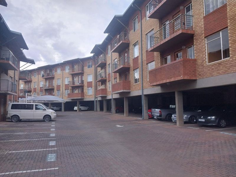 Exterior view of a multi-story apartment complex featuring brick facade, private balconies, and ground-level covered parking bays.