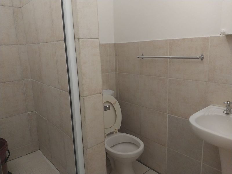 A functional bathroom featuring a shower enclosure, pedestal basin, and toilet with neutral wall tiling.