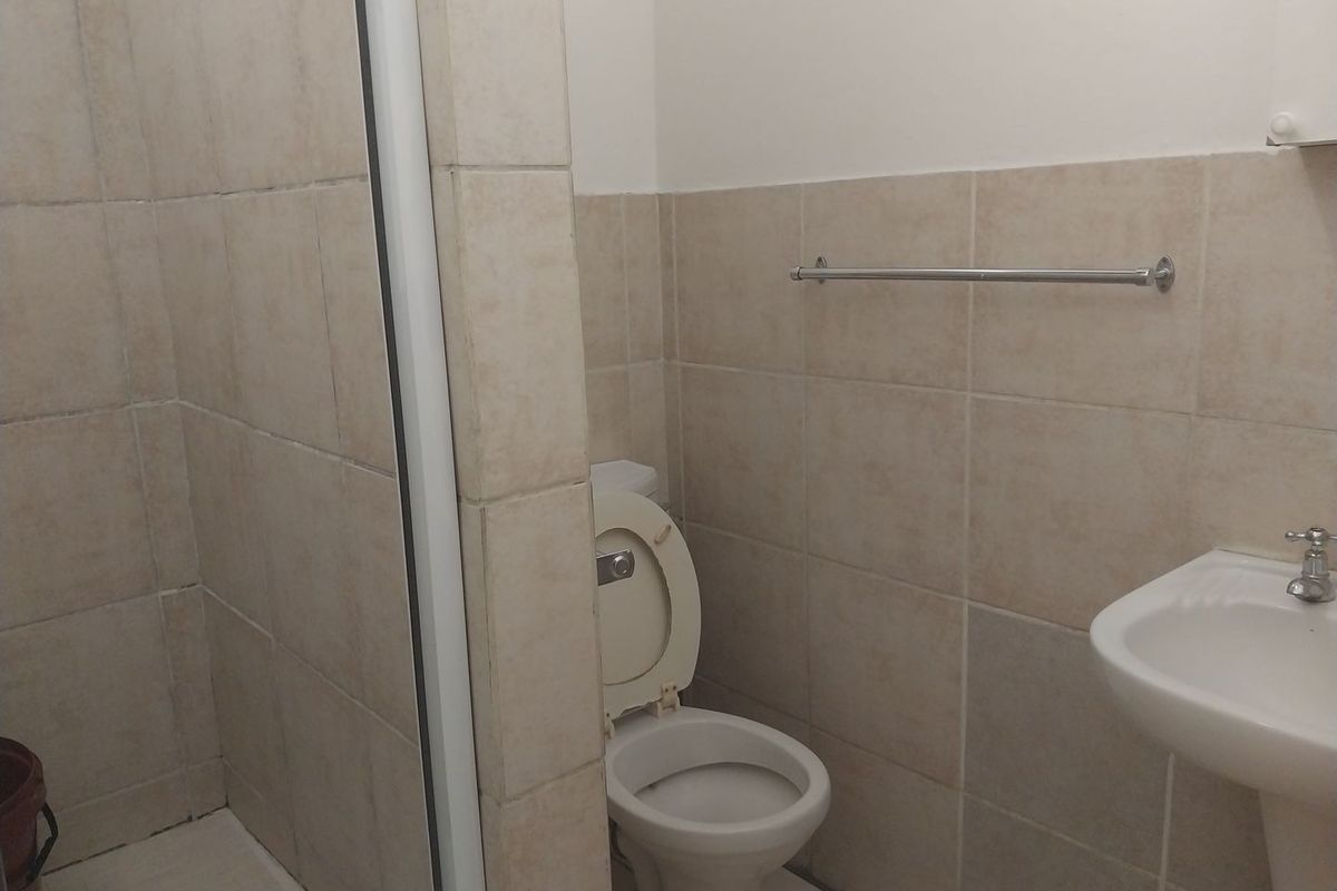 A functional bathroom featuring a shower enclosure, pedestal basin, and toilet with neutral wall tiling.