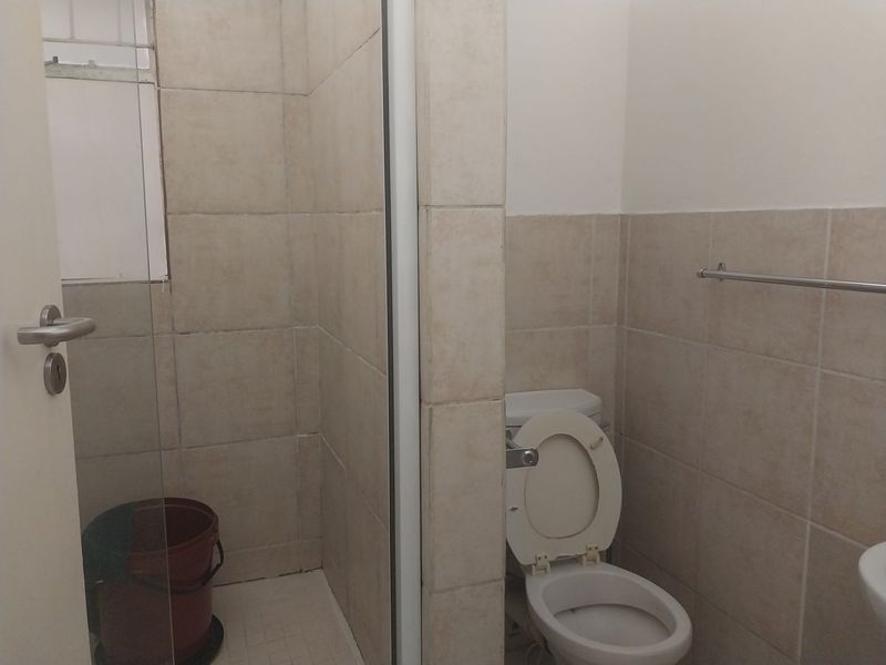 A functional bathroom featuring a shower enclosure, ceramic wall tiling, and a standard toilet with a wall-mounted towel rail.