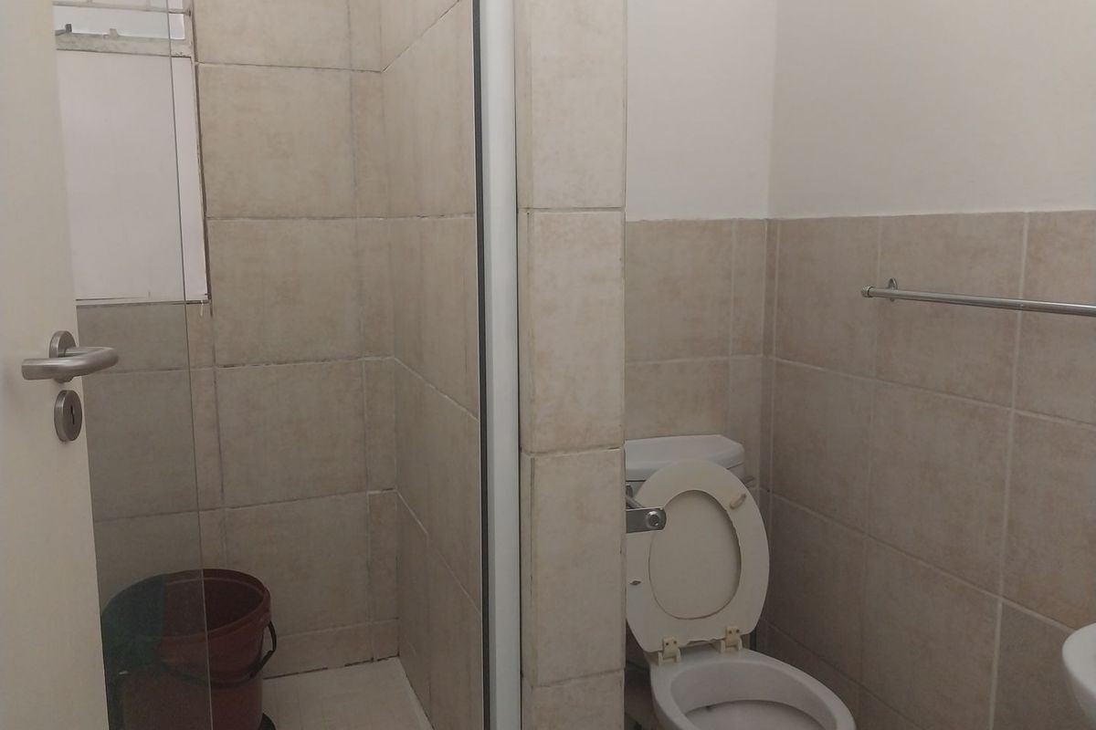 A functional bathroom featuring a shower enclosure, ceramic wall tiling, and a standard toilet with a wall-mounted towel rail.