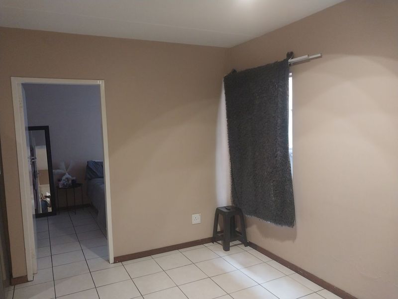 A simple, neutrally painted bedroom featuring tiled flooring and a doorway leading to an adjacent room.