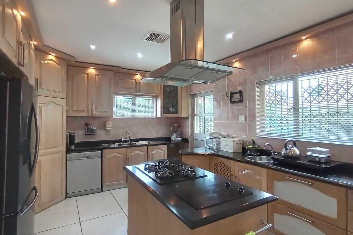 A functional kitchen featuring light wood cabinetry, dark granite countertops, a central island with a gas hob, and tiled flooring.