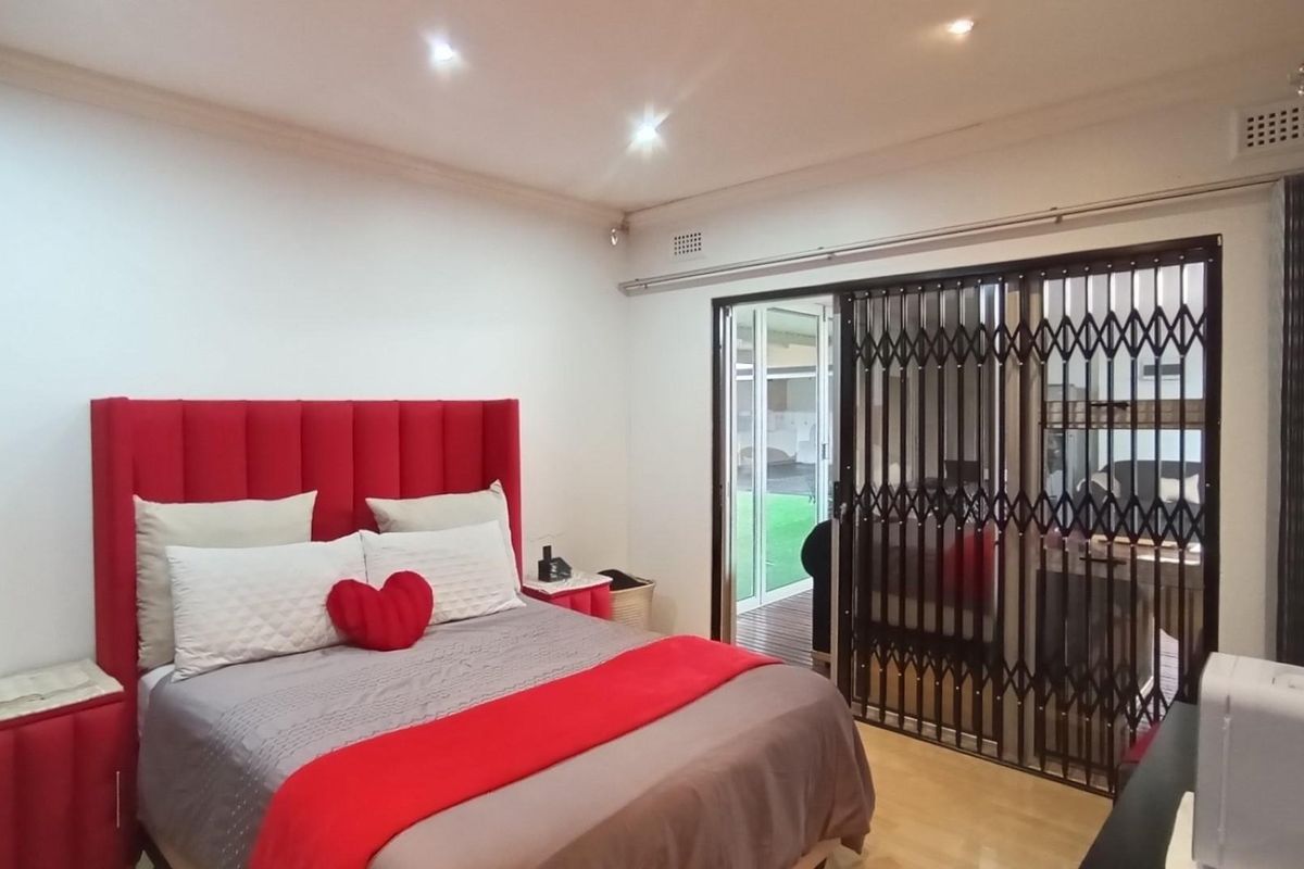 A well-maintained bedroom featuring laminate flooring, recessed downlighting, and a sliding glass door with an integrated security gate leading to the exterior.