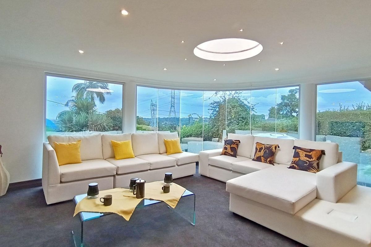 Spacious living room featuring a unique circular skylight, recessed lighting, and expansive curved floor-to-ceiling windows offering panoramic views.