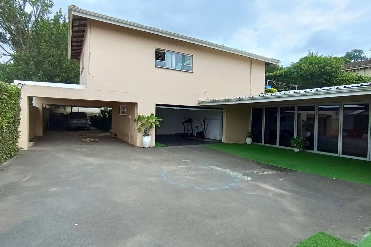 Rear exterior view featuring a covered carport, garage space, and a paved driveway area with artificial turf accents and large sliding glass doors.