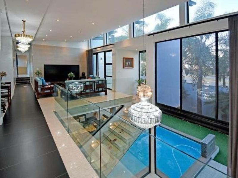 Spacious open-plan living area featuring high ceilings, large floor-to-ceiling windows, modern glass balustrades, and a view overlooking the indoor swimming pool.