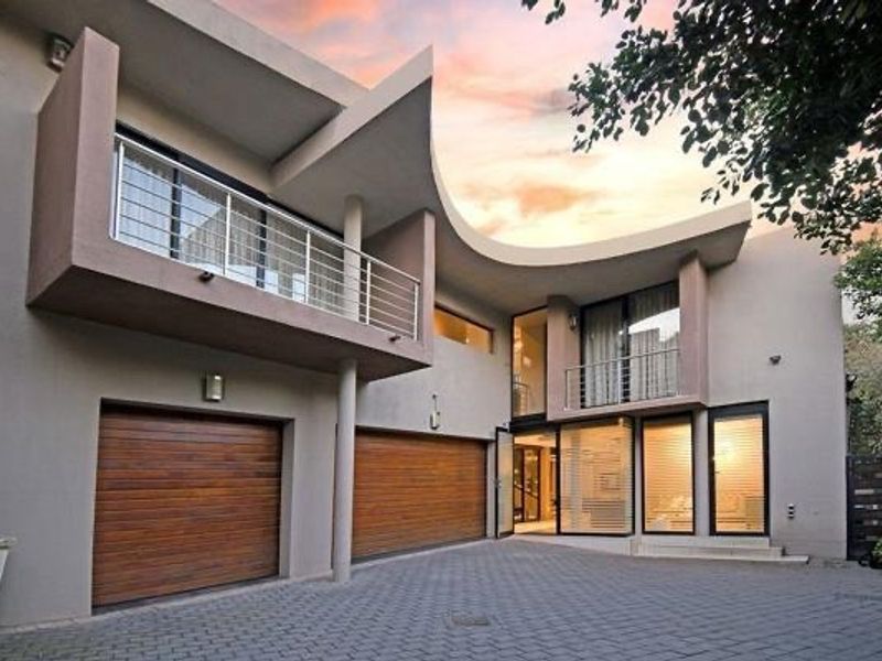 Modern architectural home exterior featuring a distinctive curved roofline, double timber garage doors, and a balcony with stainless steel balustrades.