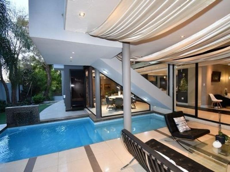 A modern outdoor pool area featuring a tiled patio, integrated water feature, and seamless transition to the interior living spaces through large sliding glass doors.