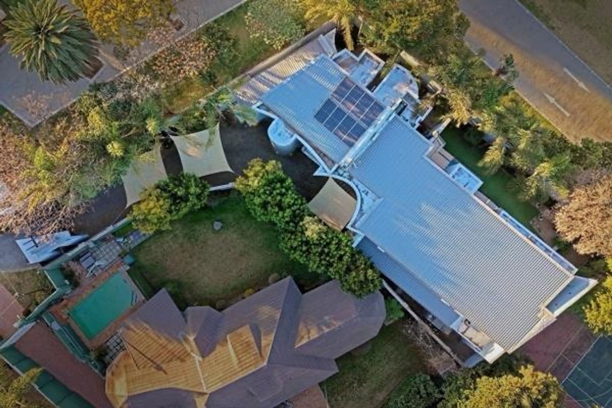 Aerial view of the property showcasing the main dwelling with solar panels, a swimming pool, landscaped garden areas, and shade sails.