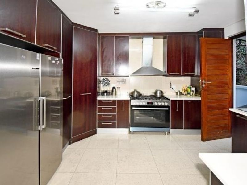A functional kitchen featuring dark wood cabinetry, stainless steel appliances including a gas stove and extractor fan, and light-colored tiled flooring.