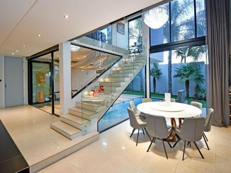 Modern open-plan living area featuring a striking glass staircase, floor-to-ceiling windows, and seamless transition to the outdoor pool and garden area.