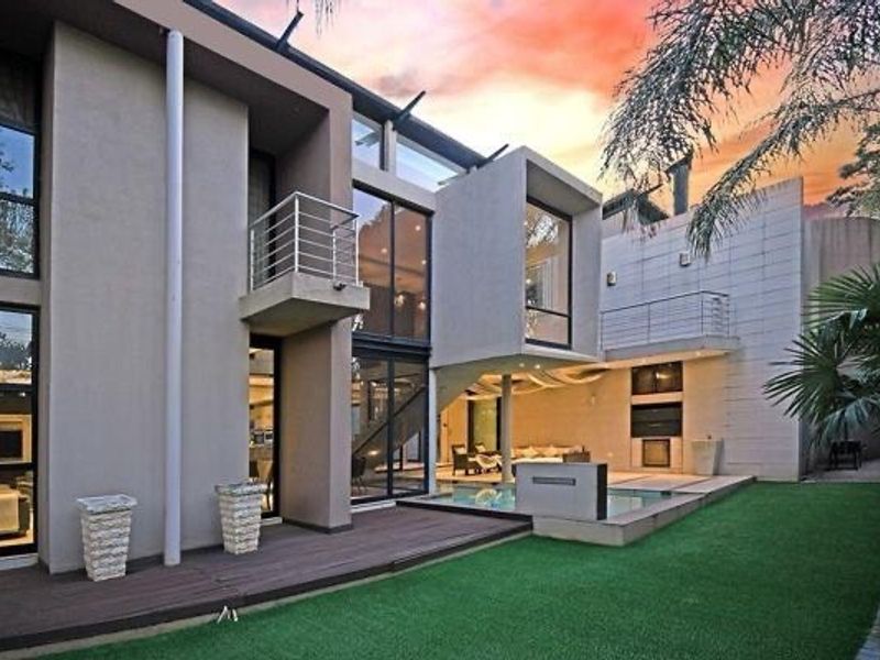 Modern multi-level rear exterior featuring a swimming pool, timber decking, balcony, and outdoor fireplace set against a landscaped garden.