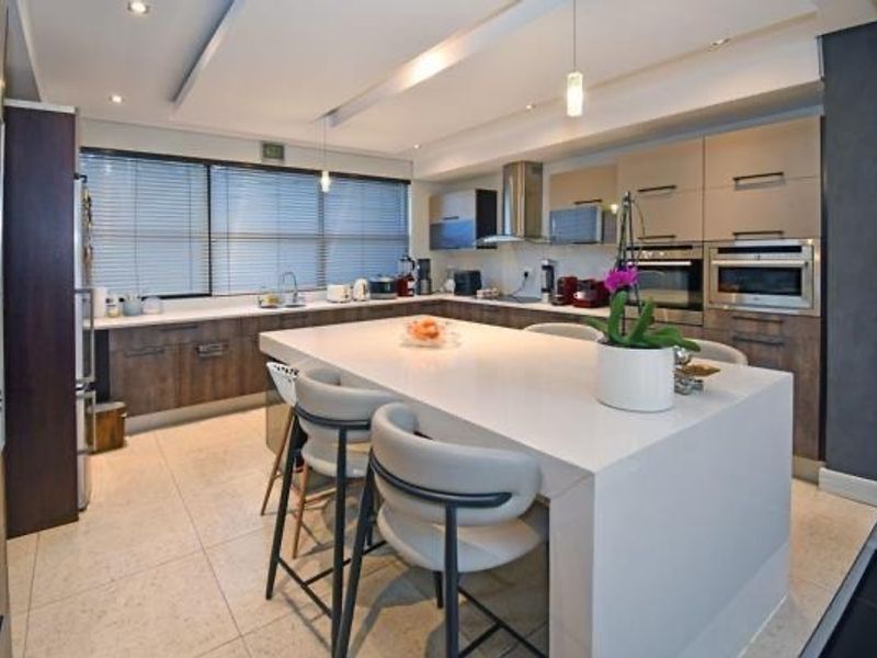 Modern kitchen featuring a large central island with stone countertops, integrated appliances, sleek cabinetry, and contemporary recessed and pendant lighting.