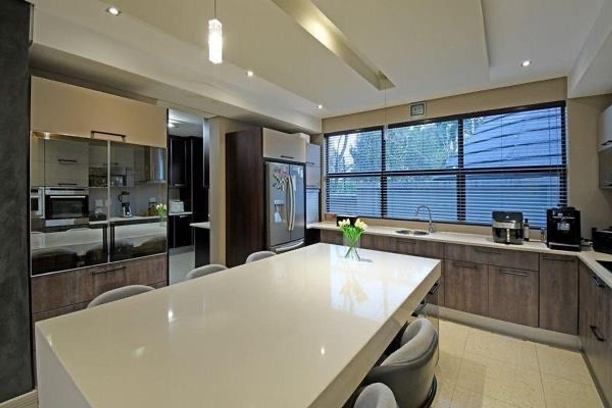 Modern kitchen featuring a large quartz island, sleek veneer cabinetry, built-in oven, and high-quality finishes with ample natural light.