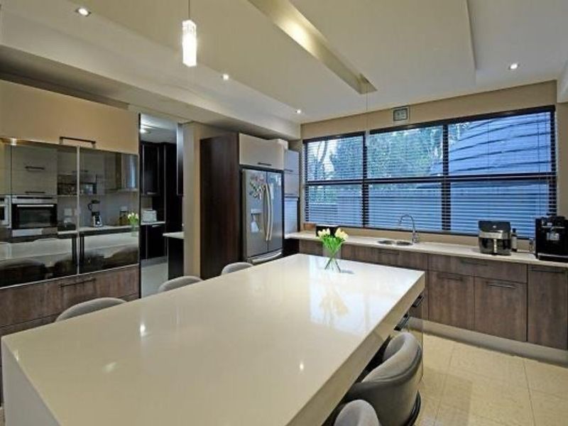 Modern kitchen featuring a large quartz island, sleek veneer cabinetry, built-in oven, and high-quality finishes with ample natural light.