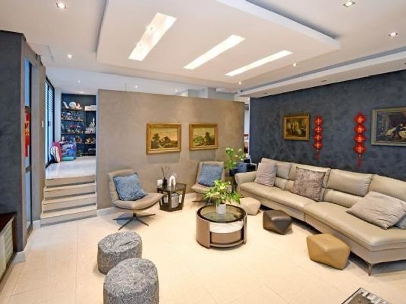 A well-maintained living room featuring a modern dropped ceiling with recessed lighting, tiled floors, and a stylish textured feature wall.