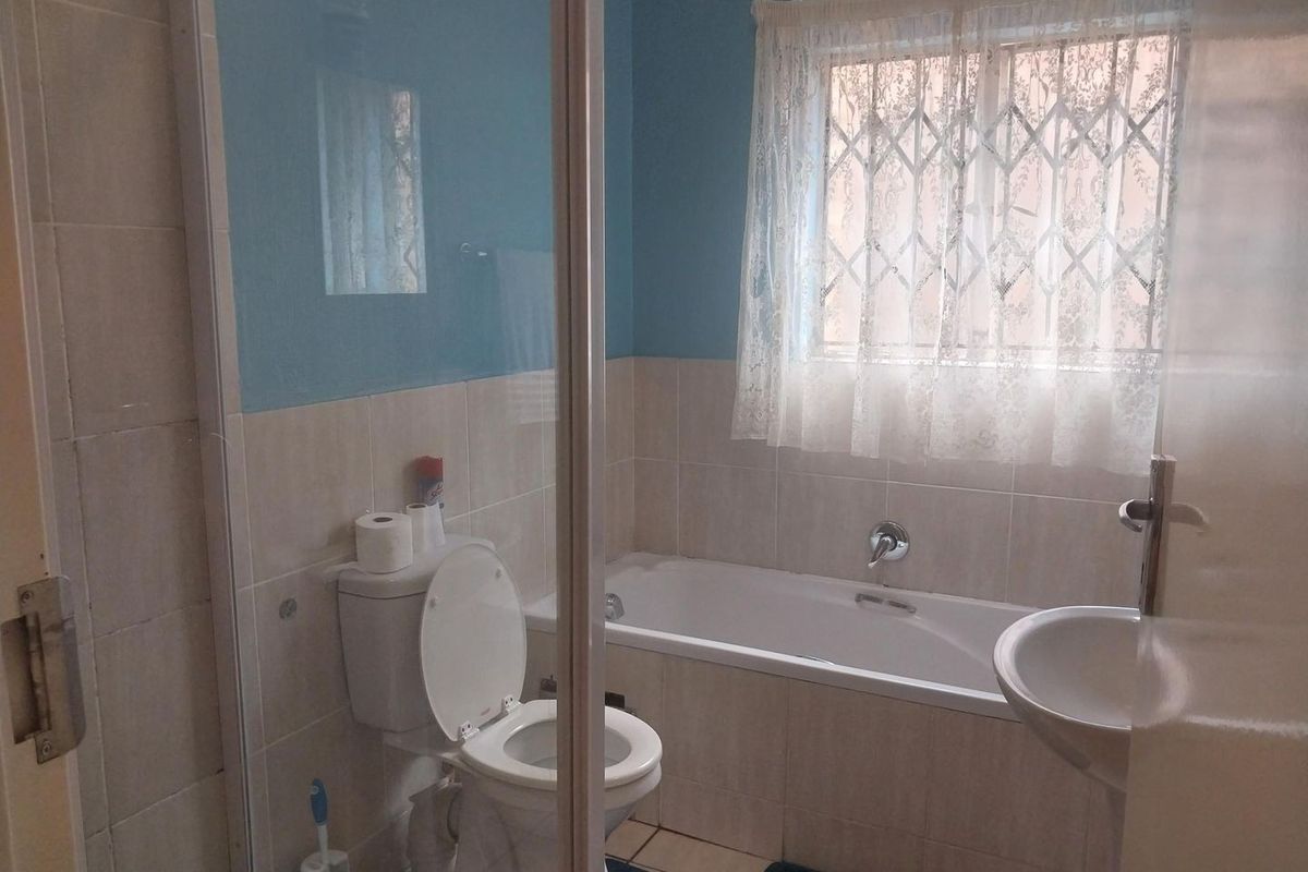 A functional bathroom featuring a bathtub, pedestal basin, toilet, and a shower enclosure with tiled finishes and a window with security bars.