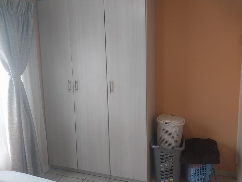 A bedroom featuring a light-toned built-in wardrobe with modern handles and tiled flooring.