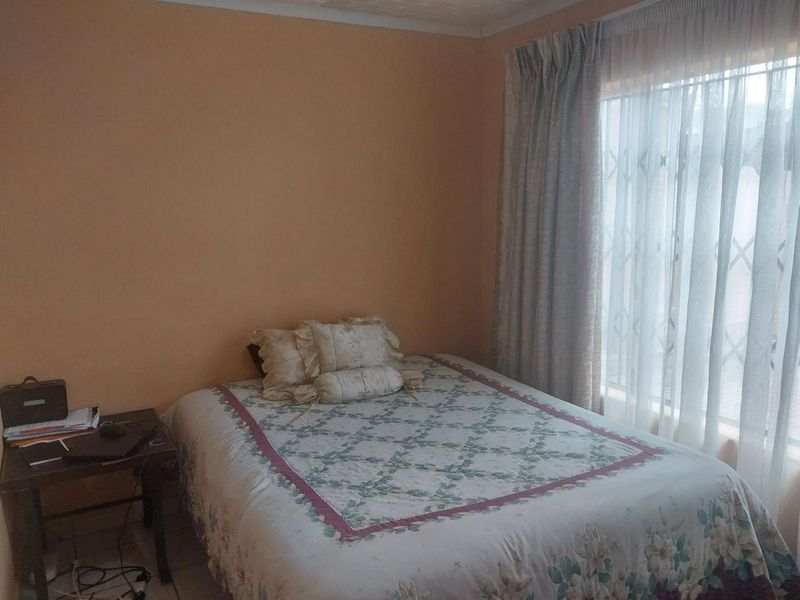 A standard bedroom featuring tiled flooring and a window fitted with a security gate and curtains.