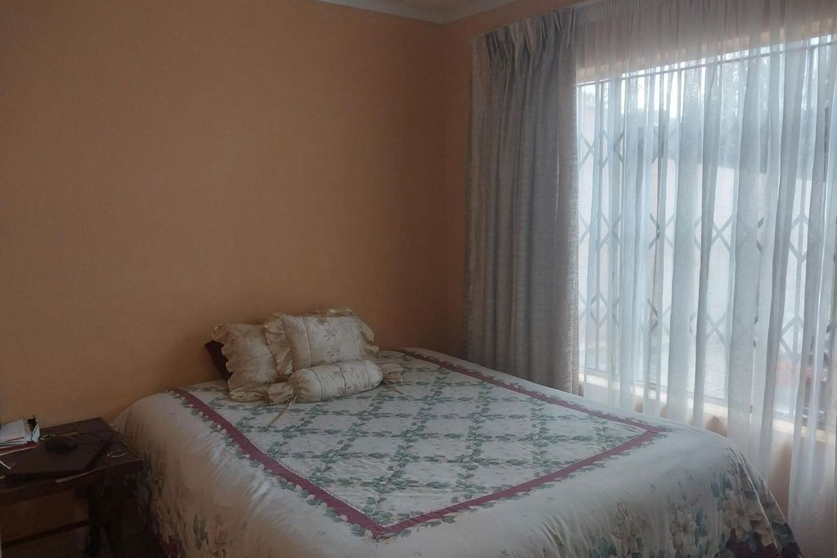 A bedroom featuring a large window with a fitted security gate and curtain tracks, providing natural light.