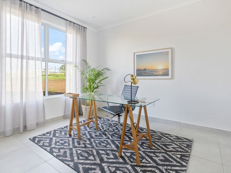 A bright and modern home office featuring neutral tiled flooring, clean white walls, and a large window providing natural light and rural views.
