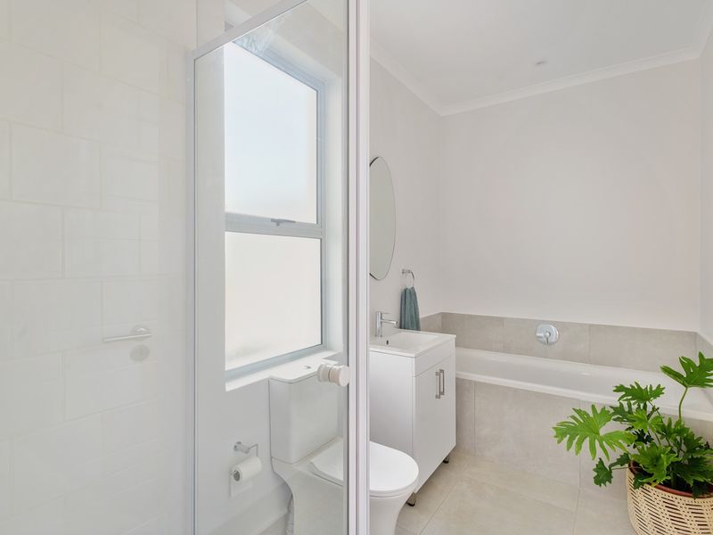 A clean, modern bathroom featuring a shower enclosure, a bathtub with tiled surround, a vanity unit, and a frosted window for natural light.