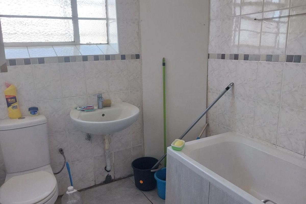 A functional bathroom featuring a bathtub, pedestal basin, and toilet with tiled finishes and an obscured glass window for privacy.