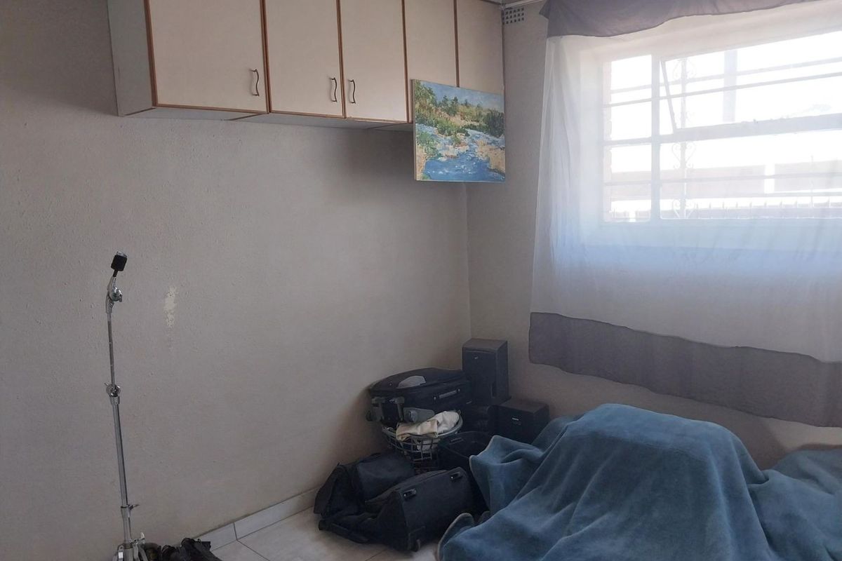A bedroom featuring built-in overhead storage cabinetry, tiled flooring, and a window fitted with security bars.