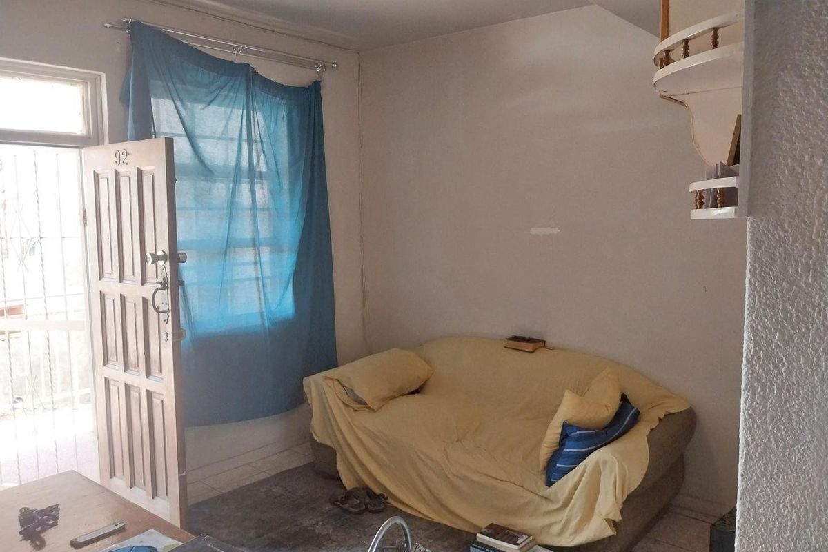 A compact living area featuring tiled flooring, a security entrance door, and built-in wall shelving, requiring cosmetic updates to improve its overall appeal.