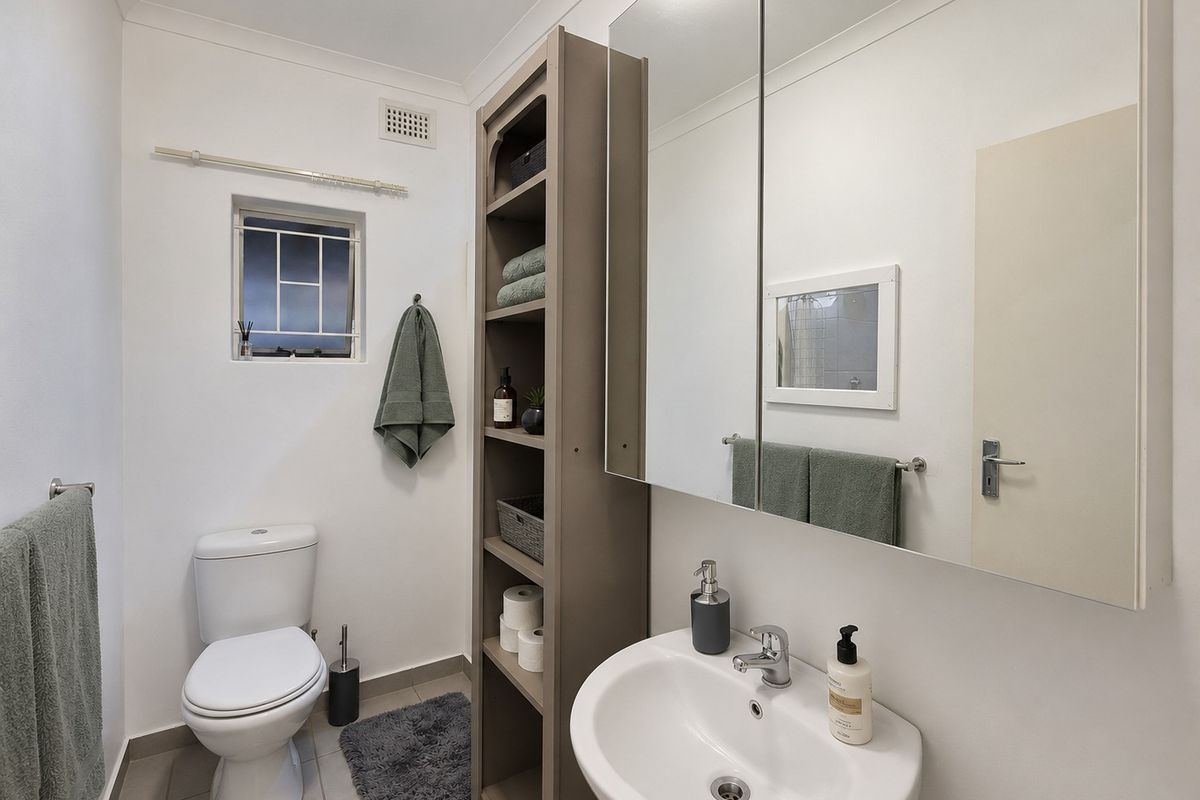 A clean and functional bathroom featuring a pedestal basin, mirrored medicine cabinet, and a standard toilet with tiled flooring.