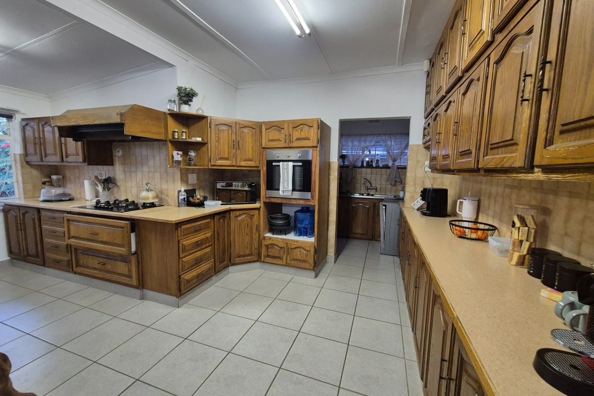 Spacious kitchen featuring extensive wooden cabinetry, built-in oven, gas hob, and tiled flooring, offering a functional layout with a separate scullery area.