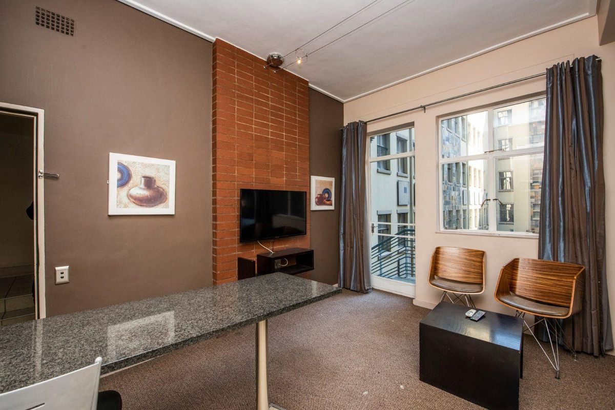 Living room featuring an exposed brick accent wall, granite breakfast bar, and large windows providing natural light and balcony access.