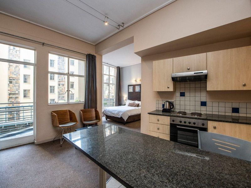 Open-plan apartment layout featuring a functional kitchen with granite countertops and integrated appliances, flowing into a bedroom area with large windows.