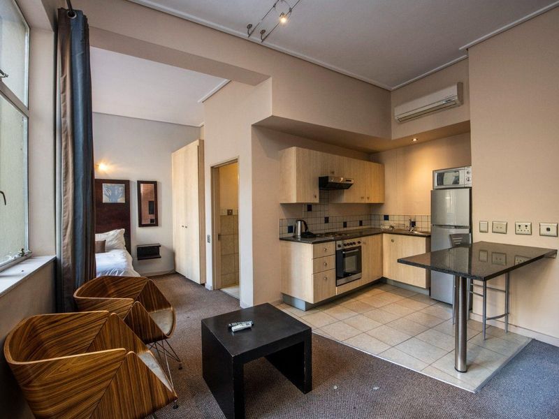 Open-plan studio apartment featuring a compact kitchen with built-in appliances, a breakfast bar, and an integrated bedroom area with built-in storage.