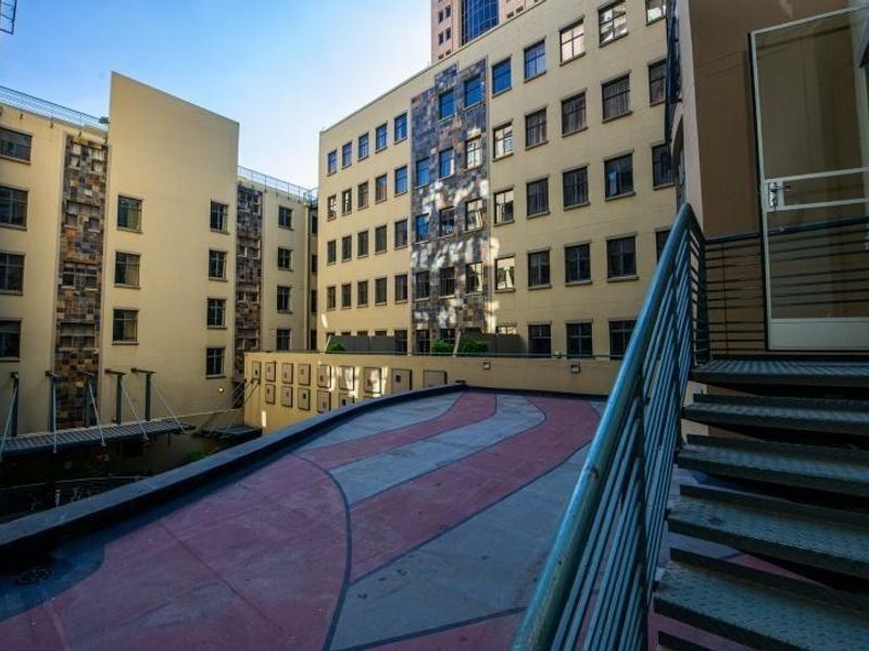 An exterior view of an apartment complex courtyard featuring a metal staircase and a paved terrace area between building wings.